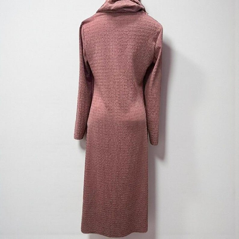 May include: A long, mauve-colored dress with a cowl neck and long sleeves. The dress has a textured knit pattern and a straight silhouette. The dress is made of a soft, comfortable material.