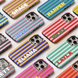 Può includere: Una collezione di custodie per telefoni colorate con motivi a righe orizzontali. Ogni custodia presenta un nome diverso in lettere bianche in grassetto. Le custodie sono in vari colori, tra cui rosa, blu, verde e giallo.