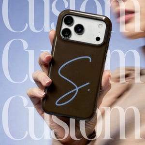 May include: A brown phone case with a light blue cursive "S" design. The case has a camera cutout and a white border around the camera. The background is a light blue with the word "Custom" in white. The text reads "Your story, your style&mdash;encased in grace." and "ARCADIA CASE."