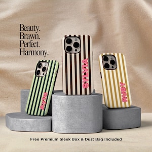 May include: Three phone cases with vertical stripe patterns in green, brown, and gold, each with a name in pink. The cases are displayed on gray pedestals against a neutral background. Text reads "Beauty. Brawn. Perfect. Harmony."