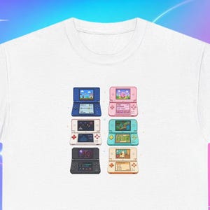 Könnte beinhalten: Ein weißes T-Shirt mit kurzen Ärmeln und einem Grafikdruck von sechs tragbaren Spielkonsolen, die in zwei Spalten angeordnet sind. Die Konsolen sind in Blau, Pink, Weiß, Türkis, Schwarz und Beige dargestellt, jeweils mit einem Spielbildschirm.