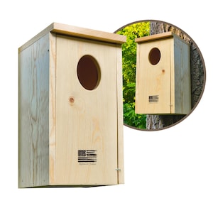 May include: A light-colored wooden birdhouse with a large circular entry hole. The birdhouse has a rectangular shape with a sloped roof and a small door. The American flag is printed on the front. The words "Approved Outdoor" are printed below the flag.