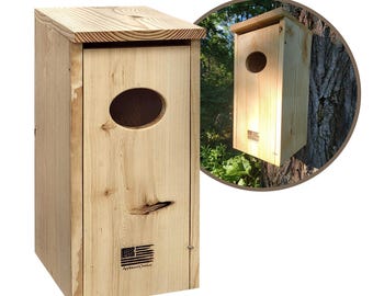 May include: A rectangular wooden birdhouse with a slanted roof and an oval entrance hole. The birdhouse is made of light-colored wood and features the American flag and the text "Approved Outdoor" printed on the front.