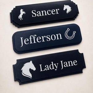 May include: Three rectangular black signs with decorative edges. The top sign features a rearing horse and the text Sancer. The middle sign displays the text Jefferson and a horseshoe. The bottom sign shows a horse head and the text Lady Jane.