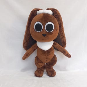 May include: A brown plush bunny toy with large, expressive eyes and long, floppy ears. The bunny has a white bib and a small white bow on its head. The toy is standing upright, with its arms and legs extended, and is made of soft, plush material.
