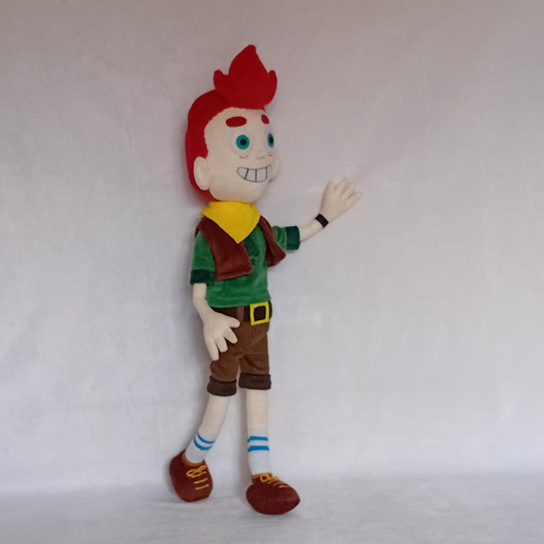 May include: A plush doll of a cartoon character with red hair, a yellow neckerchief, and a green shirt. The doll is wearing brown shorts, brown shoes, and blue and white striped socks. The doll is waving with its right hand.