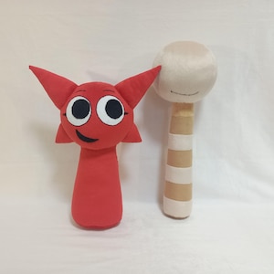 Puede incluir: Un peluche rojo con grandes ojos blancos y negros, orejas puntiagudas y una boca sonriente, junto a un peluche a rayas beige y blancas con cabeza redonda y cuerpo cilíndrico, ambos fabricados con texturas de tela suave.