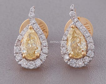 May include: A pair of pear-shaped yellow diamond earrings set in white gold, each surrounded by a halo of small round white diamonds. The earrings feature a curved top accent and are marked with 18K on the gold earring backs. AVINA JEWELS text.