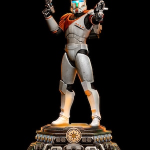 Puede incluir: Una figura coleccionable detallada de un soldado clon comando con armadura blanca y naranja y una visera azul brillante. El soldado sostiene dos blásteres en una pose de combate, sobre una base mecánica circular con un emblema dorado.