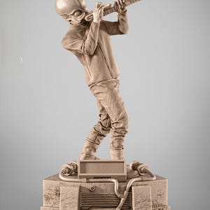 Puede incluir: Una escultura beige de un extraterrestre tocando un instrumento largo y rectangular. La figura está posada sobre una base cuadrada con un altavoz y otros detalles. La escultura es detallada y parece estar hecha de un material similar a la piedra.