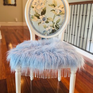 May include: An elegant white chair with a floral patterned back in blue and white. The seat is covered in light blue faux fur, and the legs are decorated with hanging crystal beads. The chair is a decorative item, suitable for a bedroom or living room.