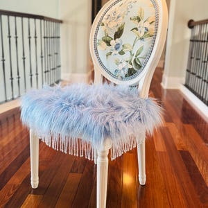 May include: An elegant white chair with a floral back and a fluffy, light blue seat. The seat has a beaded fringe. The chair's back displays a light blue floral pattern with white and blue flowers.