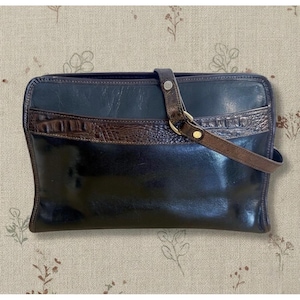 May include: A rectangular black leather handbag featuring a smooth finish and a horizontal dark brown crocodile-embossed leather strap across the upper section. The bag includes a matching brown leather shoulder strap attached with gold-tone hardware.