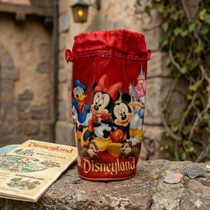 Pu&ograve; includere: Tazza souvenir rossa di Disneyland con Topolino, Minnie, Paperino e Cip e Ciop. La tazza ha una parte superiore rossa con coulisse e il logo Disneyland Resort. Una mappa di Disneyland e spille sono accanto alla tazza.
