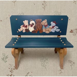 May include: A small wooden bench painted in a deep teal color with a backrest featuring a hand-painted illustration of five teddy bears in various shades of brown, cream, and blue, each wearing a small red bow, supported by natural wood legs.