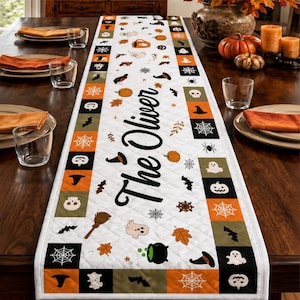 Pode incluir: Um caminho de mesa branco acolchoado com um padrão repetitivo de quadrados laranja, pretos e verde-azeitona decorados com ícones de Halloween como fantasmas, abóboras, aranhas e morcegos. O texto The Oliver está impresso em preto no centro.
