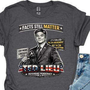 May include: Dark gray t-shirt featuring a graphic of Ted Lieu holding a gavel, with text reading "FACTS STILL MATTER" and "DEFENDING DEMOCRACY." The shirt is paired with blue jeans. The shirt also has the text "CRY MORE LIBERATE LESS" and "IT'S CALLED THE 2ND AMENDMENT NOT THE 2ND GESTION!"