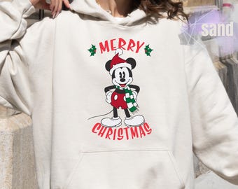 May include: Cream-colored hoodie featuring a graphic of Mickey Mouse in a Santa hat and scarf, with the words "MERRY CHRISTMAS" in red. The design is centered on the front of the hooded sweatshirt, perfect for holiday wear.