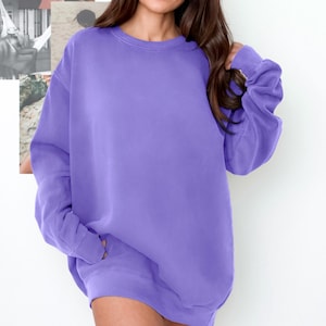 Op de afbeelding: Een effen lavendelkleurige crewneck sweatshirt. De top met lange mouwen heeft een relaxte pasvorm en geribde zoom en manchetten. Het model draagt de sweatshirt. De achtergrond is wit met een collage van afbeeldingen.