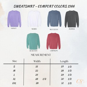 Op de afbeelding: Afbeelding van Comfort Colors sweatshirts in violet, wit, blue jean, peper, zeegroen en karmozijnrood. Een maattabel toont afmetingen in inches, met breedtes van 21 tot 28 inch (53 tot 71 cm) en lengtes van 27,5 tot 31,5 inch (70 tot 80 cm).