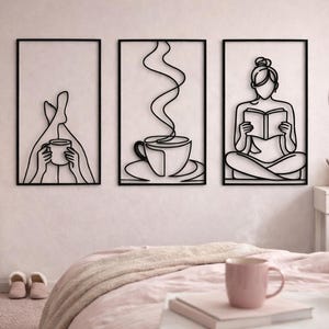 Puede incluir: Juego de tres piezas de arte mural de metal negro. Una representa a una persona con una taza, otra una taza de café con vapor y la tercera a una persona leyendo un libro. Cada pieza está enmarcada en un borde rectangular negro.