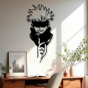 May include: Black metal wall art of a character with spiky hair and a blindfold, holding a finger to their lips. The artwork is mounted on a white wall above a wooden desk with a framed picture and a potted plant.