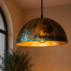 K&ouml;nnte beinhalten: Eine kuppelf&ouml;rmige Pendelleuchte mit einer verwitterten Kupferoberfl&auml;che. Das Innere ist goldfarben, und eine einzelne Gl&uuml;hbirne ist sichtbar. Die Leuchte h&auml;ngt an einem schwarzen Kabel, geeignet f&uuml;r die Innenbeleuchtung.