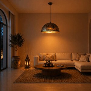 K&ouml;nnte beinhalten: Ein warmes Wohnzimmer mit einer gro&szlig;en, kuppelf&ouml;rmigen Pendelleuchte mit einem Finish in Goldoptik. Ein beiges Ecksofa, ein runder Holztisch und ein gewebter Teppich vervollst&auml;ndigen den gem&uuml;tlichen Raum. Eine Laterne und eine Topfpflanze tragen zum Ambiente bei.