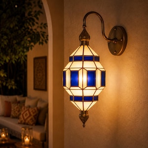 May include: A decorative wall sconce with a geometric design. The lamp features a brass finish and a stained glass shade with white and blue panels. The sconce is mounted on a beige wall, with a warm glow emanating from within.