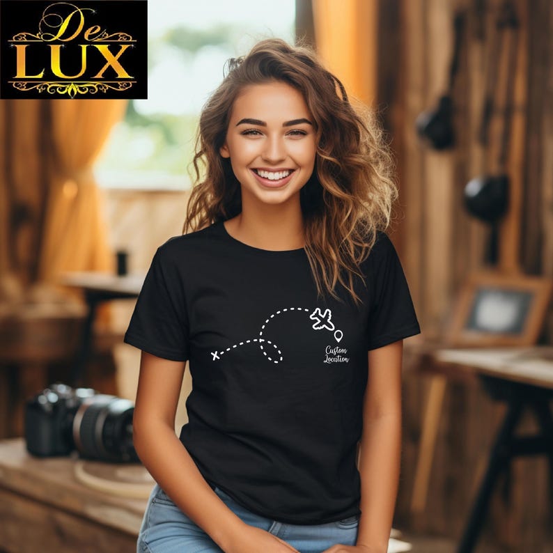 Pu&ograve; includere: T-shirt nera con grafica bianca di un aereo che segue una linea tratteggiata, con la scritta "Custom Location". Il logo De Lux &egrave; nell'angolo in alto a sinistra.