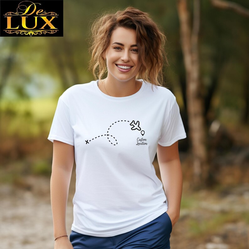Pu&ograve; includere: T-shirt bianca con grafica nera di un aereo e traiettoria a punti. Il testo "Custom Location" &egrave; sotto l'aereo. La maglietta ha maniche corte e girocollo.
