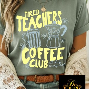 K&ouml;nnte beinhalten: Salbeigr&uuml;nes T-Shirt mit dem Text "Tired Teachers Coffee Club" in Gelb. Das Design umfasst eine Kaffeetasse und einen Espressokocher in Hellblau, mit floralen Akzenten. Der Satz "all day every day" ist ebenfalls enthalten.