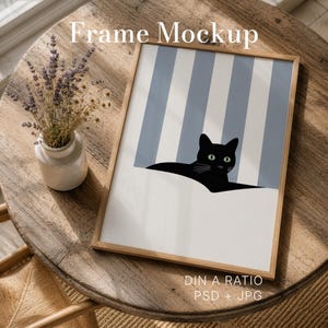 May include: A framed art print featuring a black cat with green eyes peeking out from a white surface, set against a backdrop of blue and white stripes. The frame is light brown. The words "Frame Mockup" are at the top.