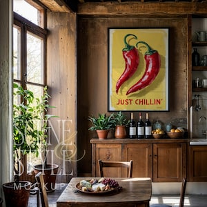 May include: A framed poster with two red chili peppers on a yellow background, with the text "JUST CHILLIN'". The poster hangs above a wooden cabinet with wine bottles and plants. A wooden table is set with food.