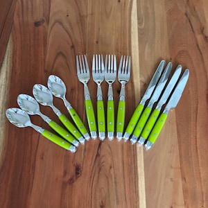 May include: A flat lay of stainless steel silverware with bright green handles. The set includes spoons, forks, and knives, arranged on a wooden surface. The silverware has a classic design with a modern color.