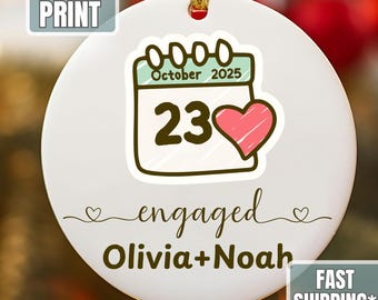 Könnte beinhalten: Runder weißer Keramik-Weihnachtsschmuck mit goldenem Faden. Er zeigt ein Kalender-Motiv mit dem Datum 23. Oktober 2025, einem rosa Herz und dem Wort "engaged" mit den Namen Olivia und Noah.