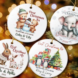 Puede incluir: Conjunto de cuatro adornos navideños redondos. Cada adorno presenta un diseño único de acuarela con el texto "First Christmas As". Los diseños incluyen osos, un elefante, conejos y pingüinos. Cada adorno tiene una cuerda dorada.