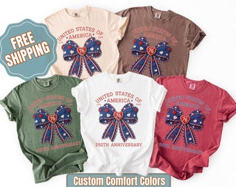 May include: A collection of t-shirts in various colors, including white, green, and red. Each shirt features a patriotic design with a bow, stars, and the text "United States of America 250th Anniversary."