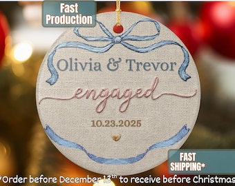 May include: Round, embroidered engagement ornament with the names "Olivia & Trevor" and the word "engaged" in cursive. The date "10.23.2025" is below. Light blue ribbon and bow design. Fast Production and Fast Shipping labels.