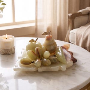 May include: A decorative set of polished light green stone fruit, including an apple, a pear, and a cluster of grapes, resting on a matching stone leaf-shaped tray. The fruit pieces feature smooth, translucent surfaces with natural veining.