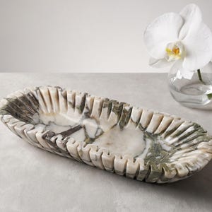 May include: An elongated oval tray carved from white and dark green marbled stone. The tray features a distinctive scalloped or fluted edge design with vertical ridges running along the entire perimeter, creating a textured, rhythmic pattern.