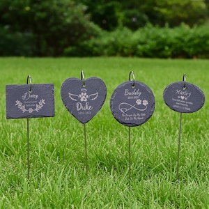 Pode incluir: Quatro estacas de jardim comemorativas para animais de estimação em ardósia cinza escuro com hastes de metal prateado. Cada estaca tem uma forma diferente: quadrada, coração, círculo e oval. As estacas são gravadas com nomes de animais de estimação, datas e frases comemorativas.