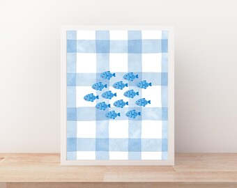 May include: A framed art print featuring a watercolor illustration of a school of blue fish. The fish are arranged in a circle against a light blue and white gingham pattern background. The artwork is displayed in a white frame.