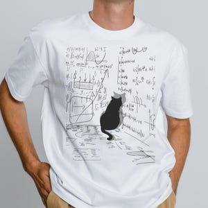Puede incluir: Camiseta blanca con una ilustración de un gato negro con un sombrero gris, sobre un fondo de ecuaciones y diagramas matemáticos. El gato está de espaldas, añadiendo un toque de fantasía al diseño. La persona lleva una gorra de camionero blanca y negra.