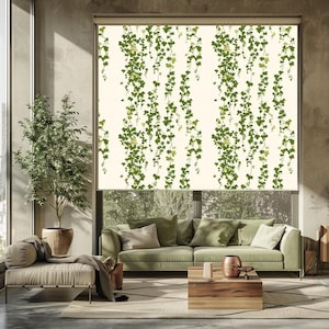 Puede incluir: Una persiana enrollable de color crema con un patrón repetido de vides de hiedra verde. Las vides caen en cascada, creando un diseño natural. La persiana está instalada en una sala de estar con un sofá verde y una mesa de centro de madera.