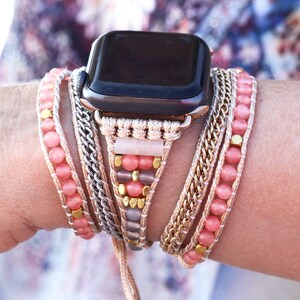 May include: A multi-strand Apple Watch band featuring pink gemstone beads, gold-tone chain, and woven cord. The band has a rose gold-tone watch case and a neutral-colored woven section with pink and gold accents.