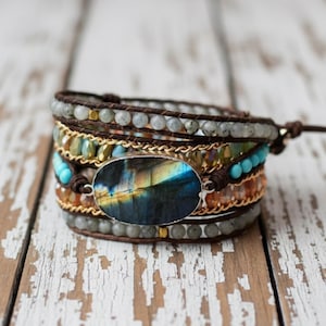 Peut inclure: Bracelet enroulé avec une grande pierre ovale de labradorite aux reflets bleus, jaunes et oranges. Le bracelet comprend plusieurs rangées de perles grises, turquoise et ambrées, avec une chaîne dorée et du cuir marron.