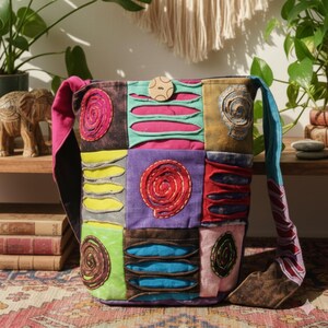 Puede incluir: Un bolso de hombro patchwork con una variedad de colores y texturas. El bolso presenta cuadrados de tela en tonos marrón, rosa, amarillo, verde, morado y azul. Cada cuadrado tiene costuras y diseños recortados únicos. Un botón de madera asegura la solapa.