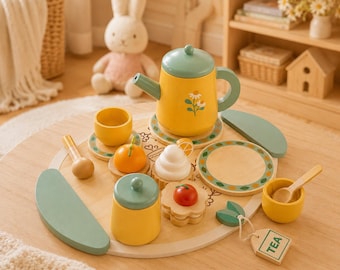 May include: A wooden toy tea set featuring a yellow teapot with a green lid and floral design, a matching yellow lidded jar, two yellow cups, a wooden spoon, a plate, and small food items including a fruit slice and a tag labeled TEA.