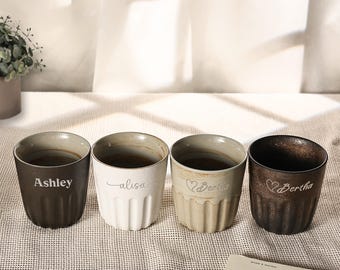 Puede incluir: Cuatro tazas de cerámica con texturas acanaladas verticales y texto personalizado. La primera es marrón oscuro con 'Ashley', la segunda blanca con 'alisa', la tercera beige claro con 'Bertha' y la cuarta marrón oscuro con 'Bertha'.